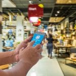 Mobile payment, Cashless society concept. Hand holding smart phone with mobile payment on screen and NFC signals icons against abstract furniture mart background.
